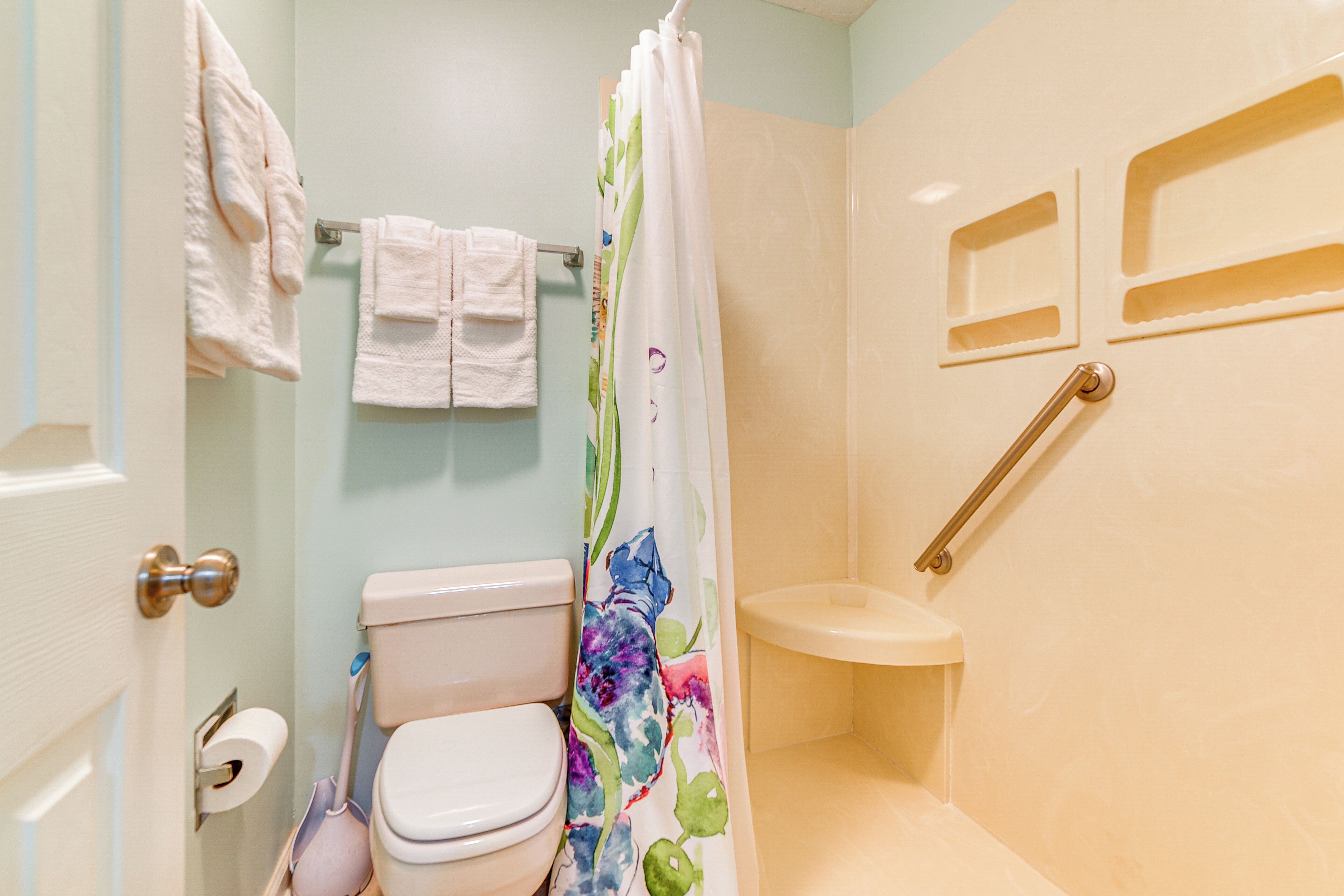 Un baño con inodoro, cortina de ducha, toallero y toallas, y barra de apoyo.