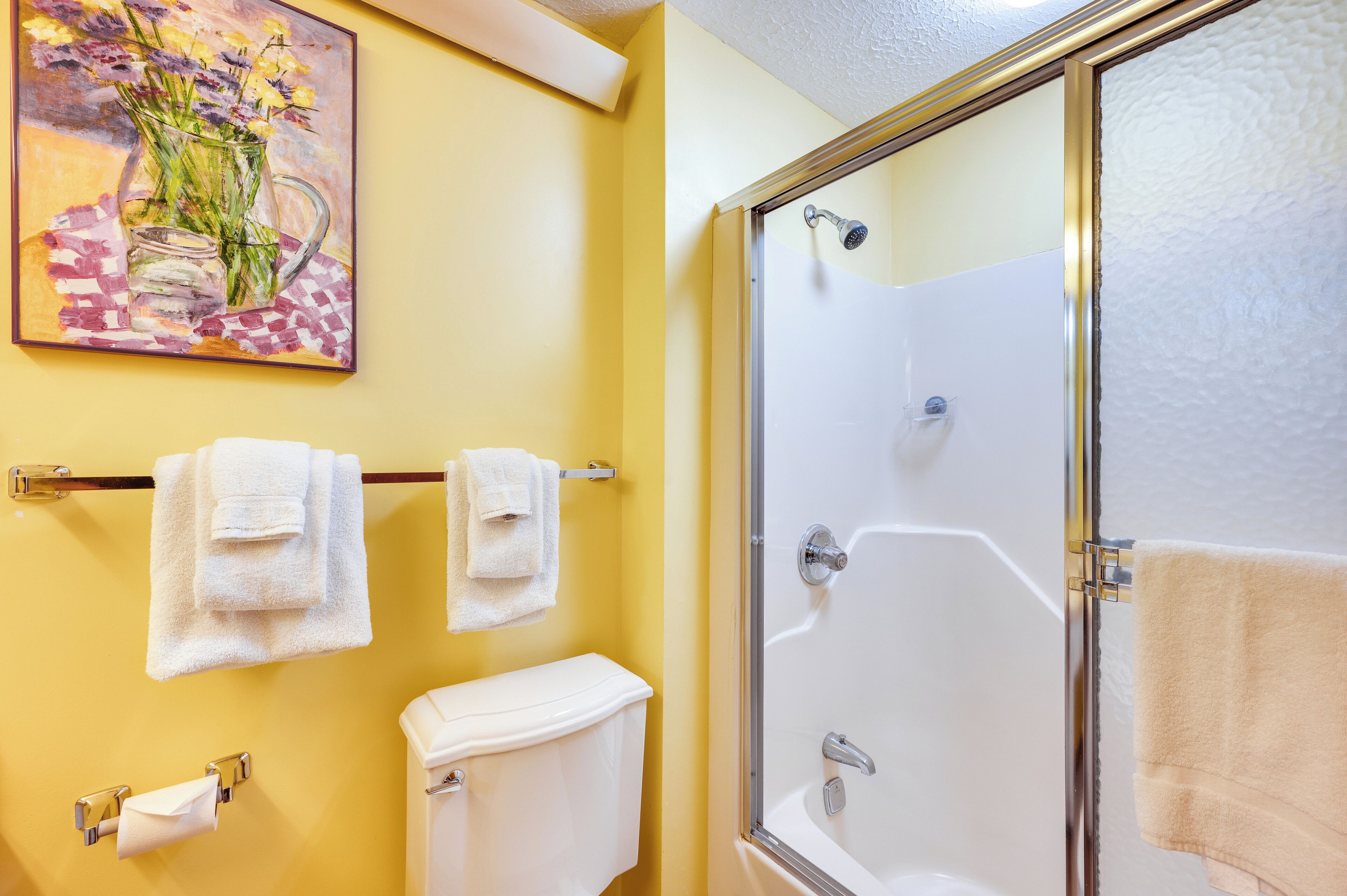 A bathroom with a shower, toilet, and a painting of flowers on the wall.