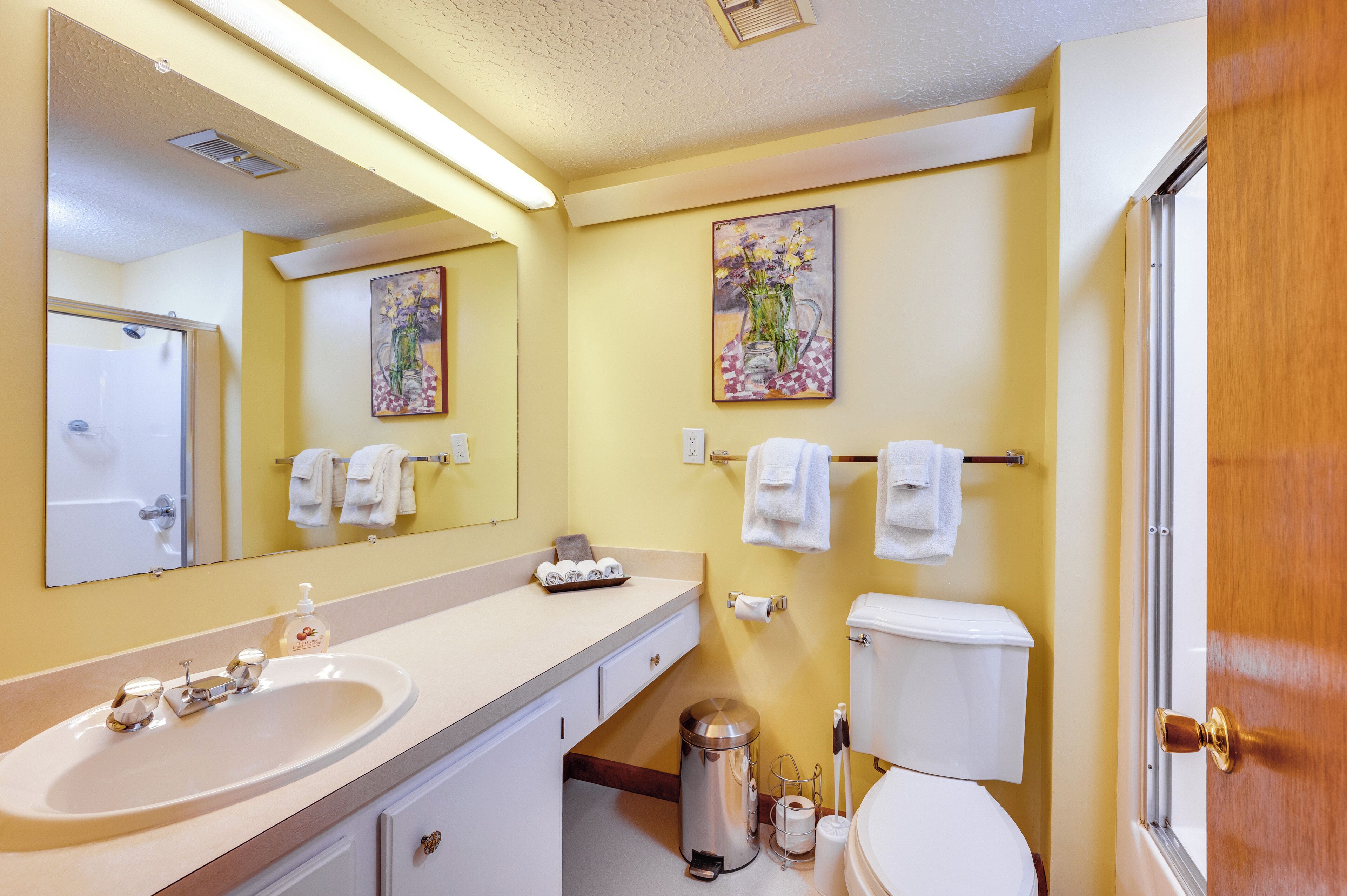 Une salle de bain équipée d’un lavabo, d’un miroir, de toilettes et d’une poubelle.