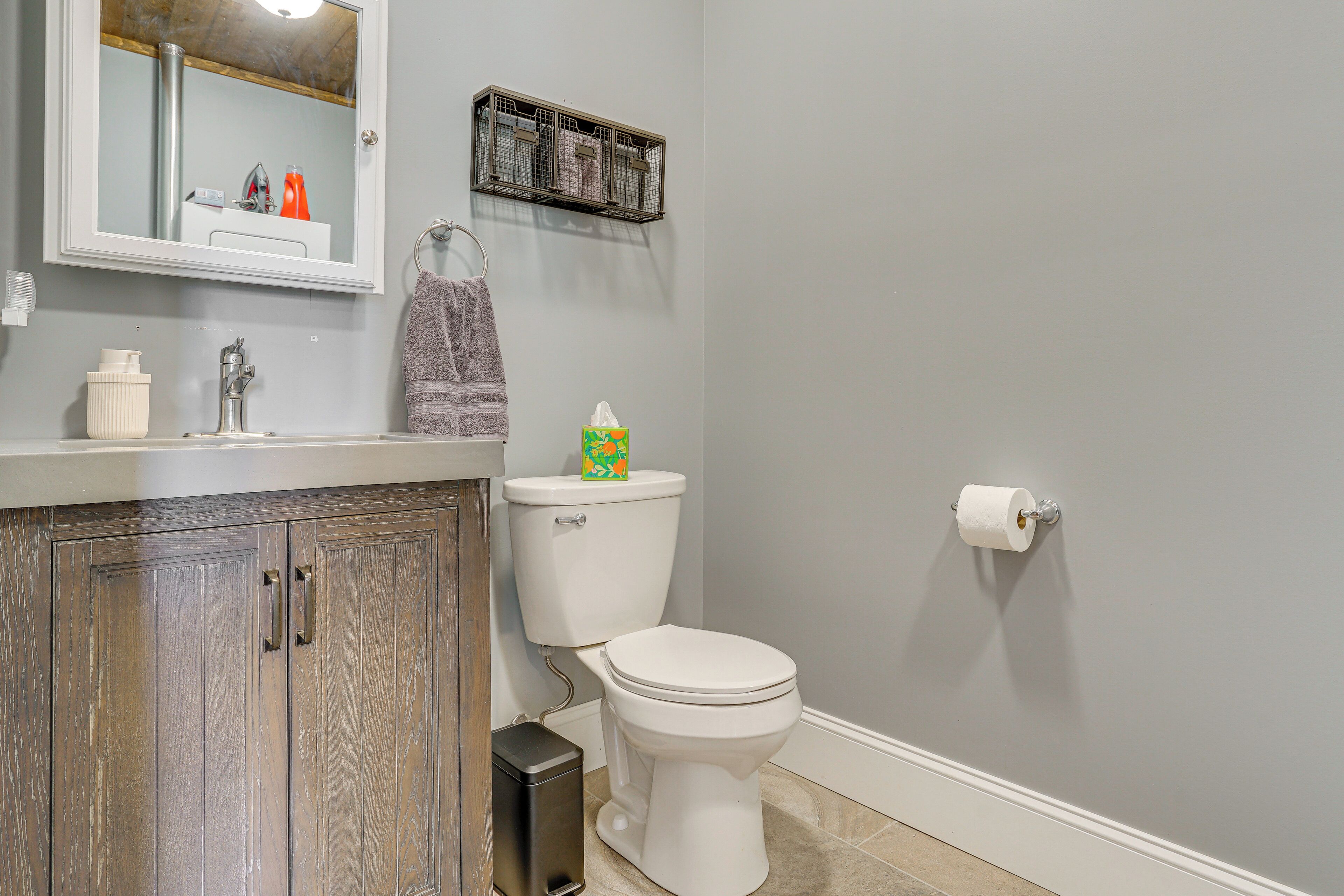 A bathroom with a wooden cabinet, a toilet, a shelf with toiletries, and a mirror.