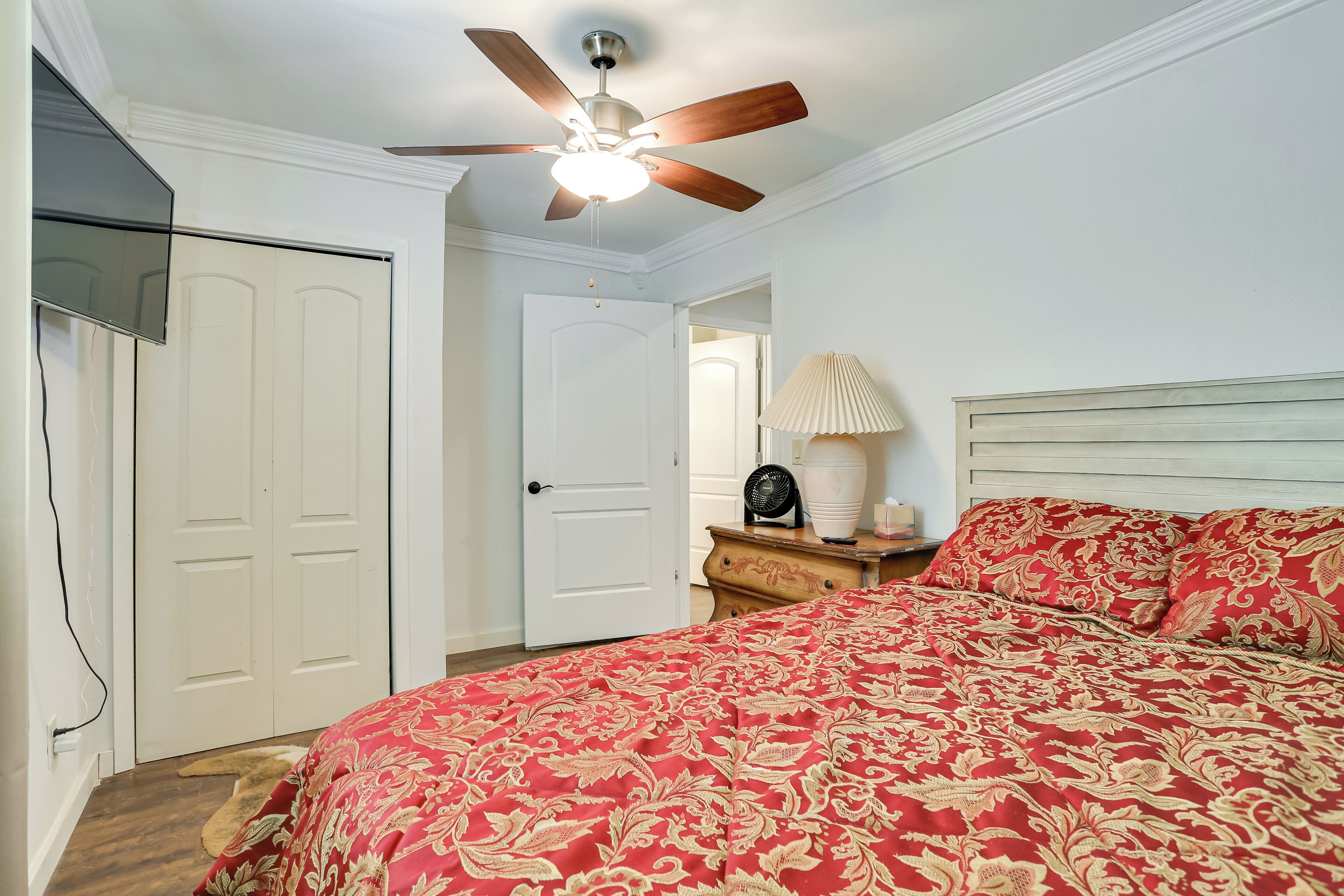 A bedroom with a bed, a ceiling fan, a nightstand, and a lamp.