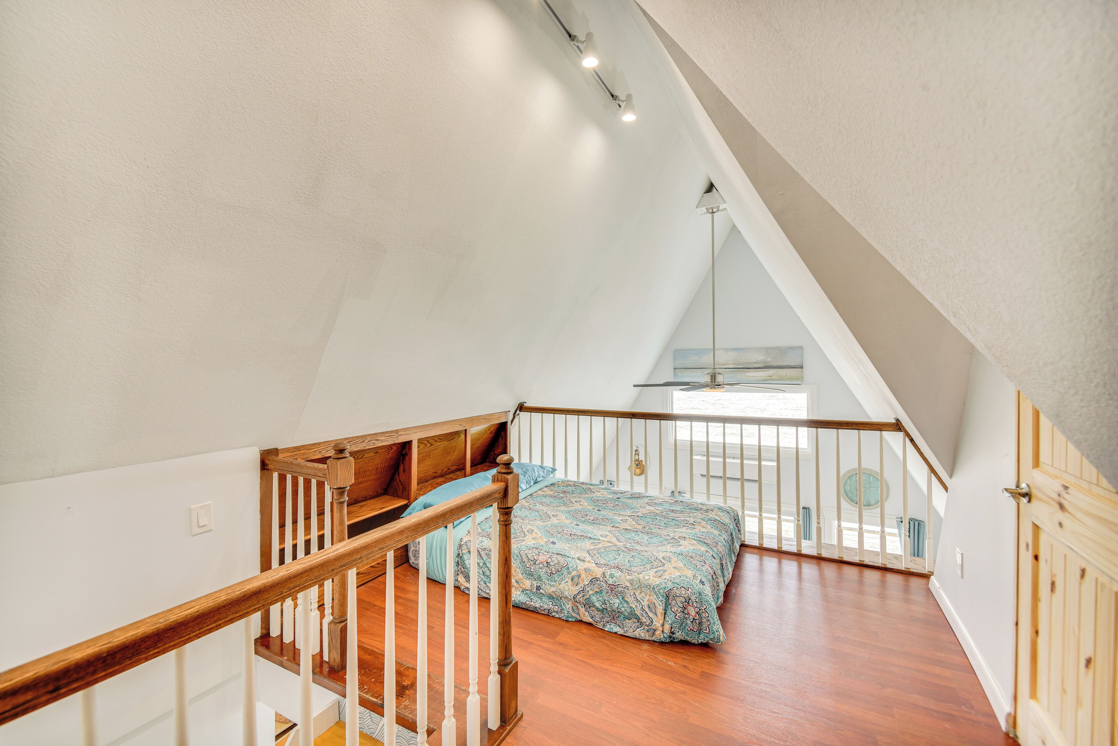 A bedroom with a wooden staircase, a bed with patterned bedding, and a view of the outdoors through a window.