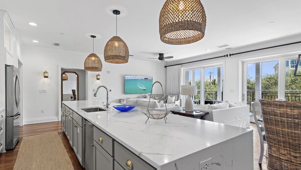 A modern kitchen with a large island, white cabinetry, and a dining area with a wicker chair. - Rooftop Comm Pool - WaterHouse 204 by Royal Destinations (Inlet Beach)