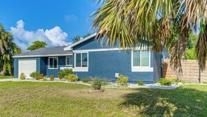 A single-story house with a blue exterior, white garage door, and a small front yard with a palm tree and shrubs. - 5 Mi to Beach: Pet-friendly Port Charlotte Home (Port Charlotte)