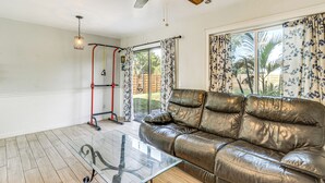 A living room with a leather sofa, a glass coffee table, a ceiling fan, and a view of the outdoors through large windows. - 5 Mi to Beach: Pet-friendly Port Charlotte Home (Port Charlotte)