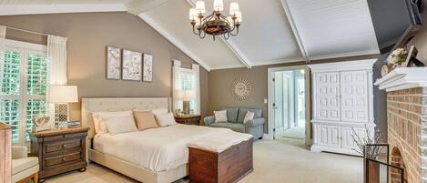 A bedroom with a large bed, a chandelier, a dresser, and a fireplace.