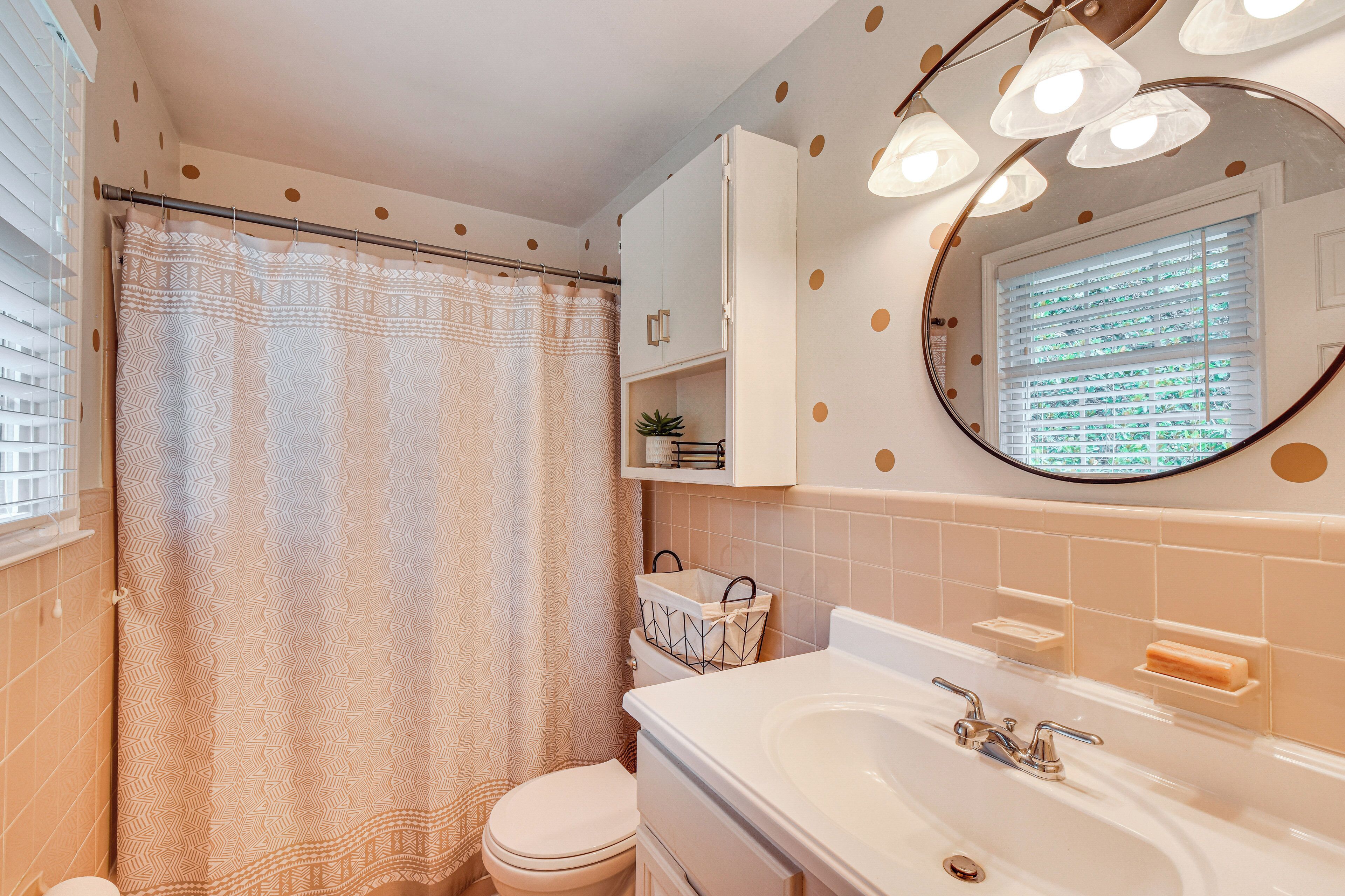 A bathroom with a shower curtain, toilet, sink, and a mirror with lights.