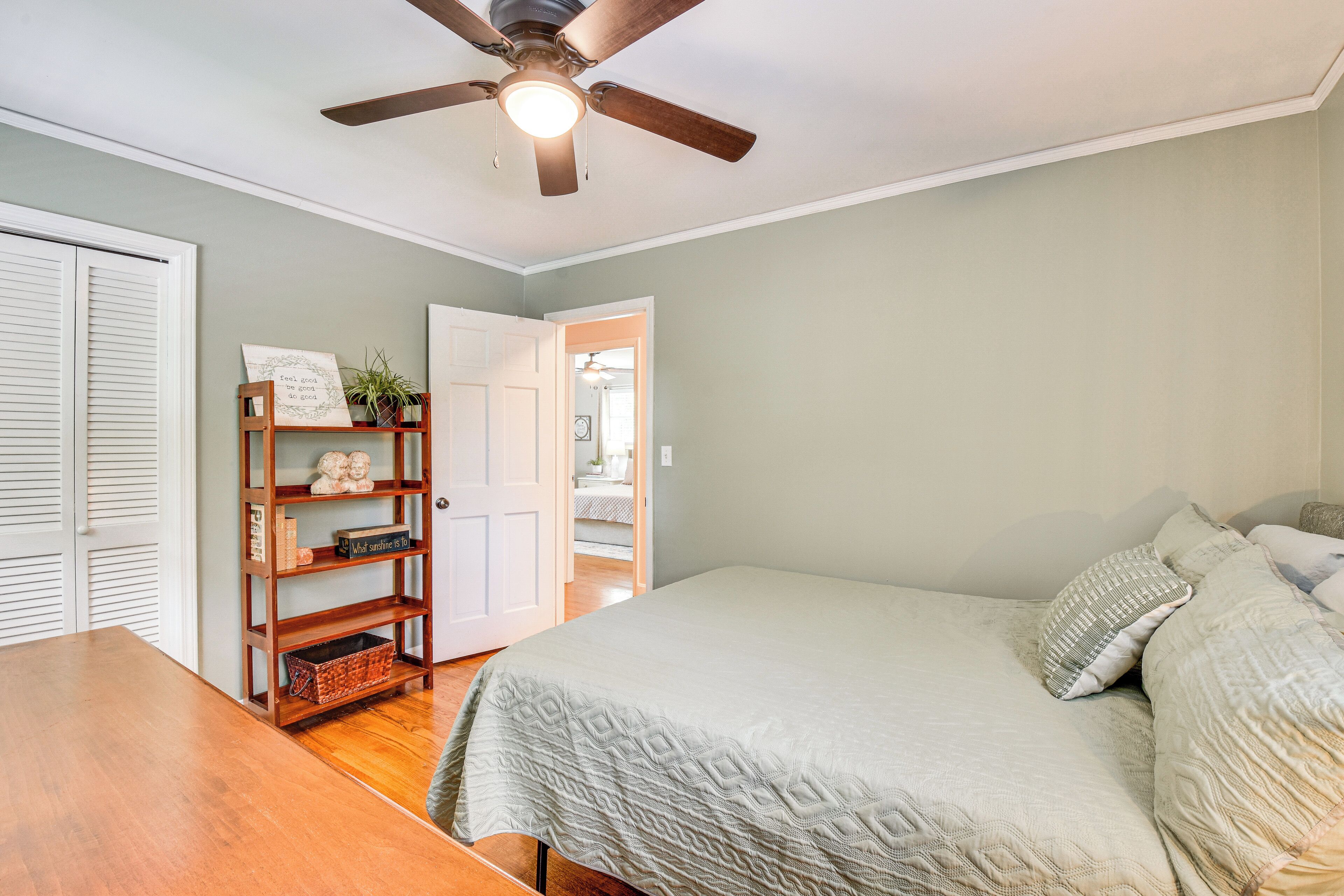 A bedroom with a bed, a wooden nightstand, a ceiling fan, and a bookshelf.
