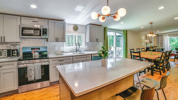 A modern kitchen with stainless steel appliances, a large island, and a dining area with wooden flooring and chairs.