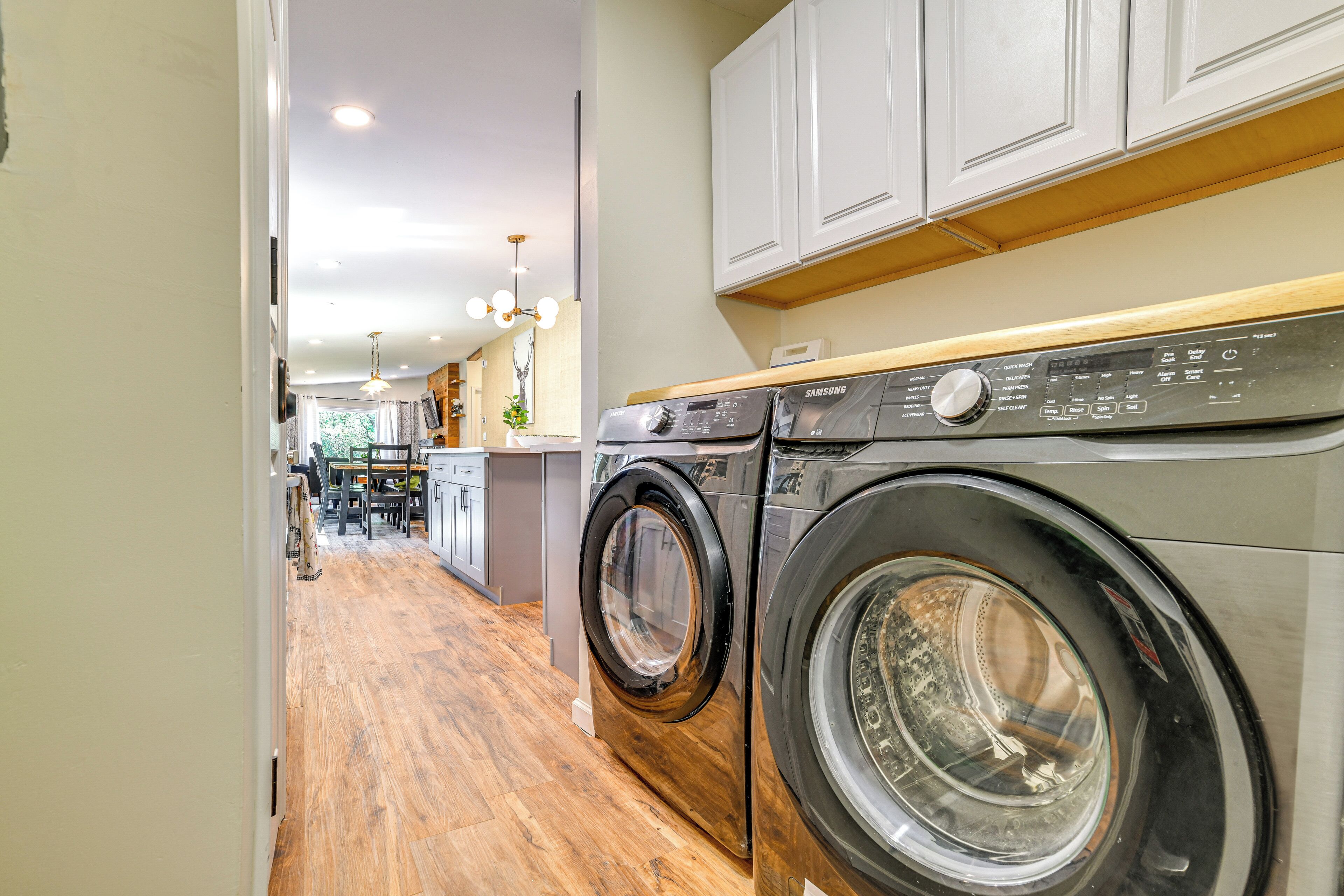A laundry area with two front-loading washing machines, wooden flooring, and white cabinetry.