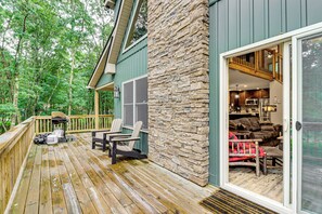 Une terrasse en bois avec des sièges d’extérieur, un mur en pierre et une vue sur l’intérieur à travers une porte vitrée.