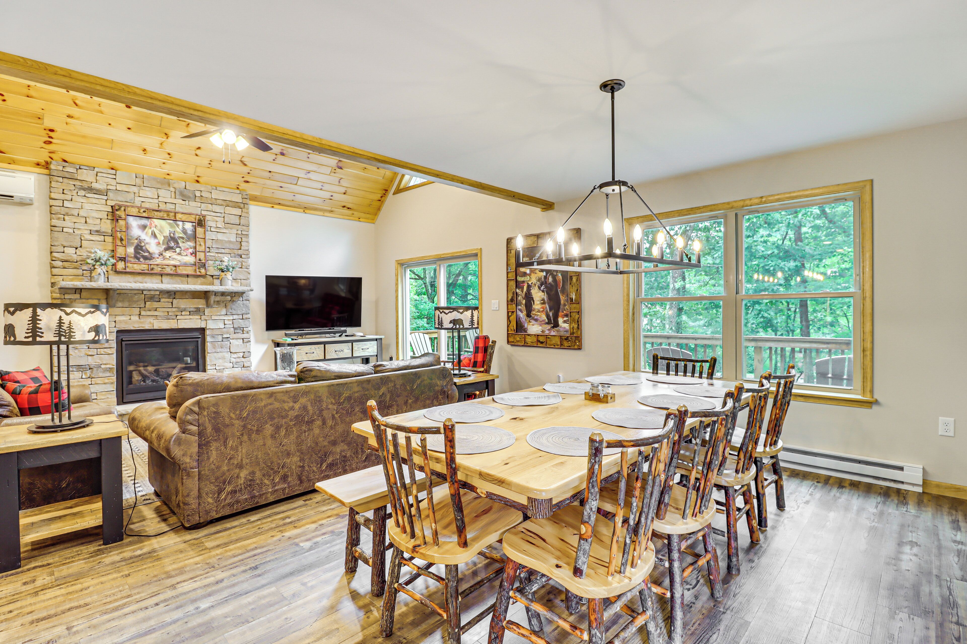 A spacious living room with a fireplace, a dining area with wooden chairs, and large windows offering a view of the outdoors.