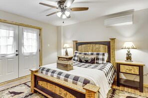 Une chambre à coucher comprenant un lit, un ventilateur de plafond, deux tables de chevet avec des lampes, un banc en bois et une porte avec des panneaux en verre dépoli.