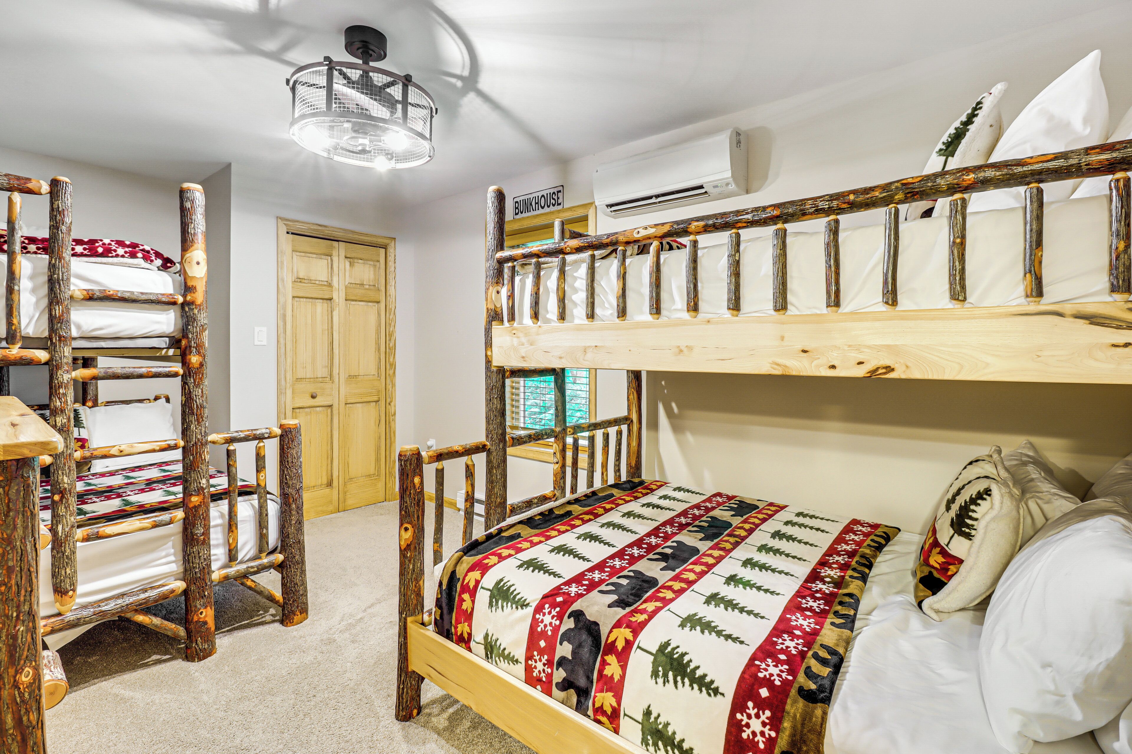 Una cama litera con estructura de madera y colcha acolchada. Se observa una silla de madera con cojín, una puerta de madera y un equipo de aire acondicionado en la pared.