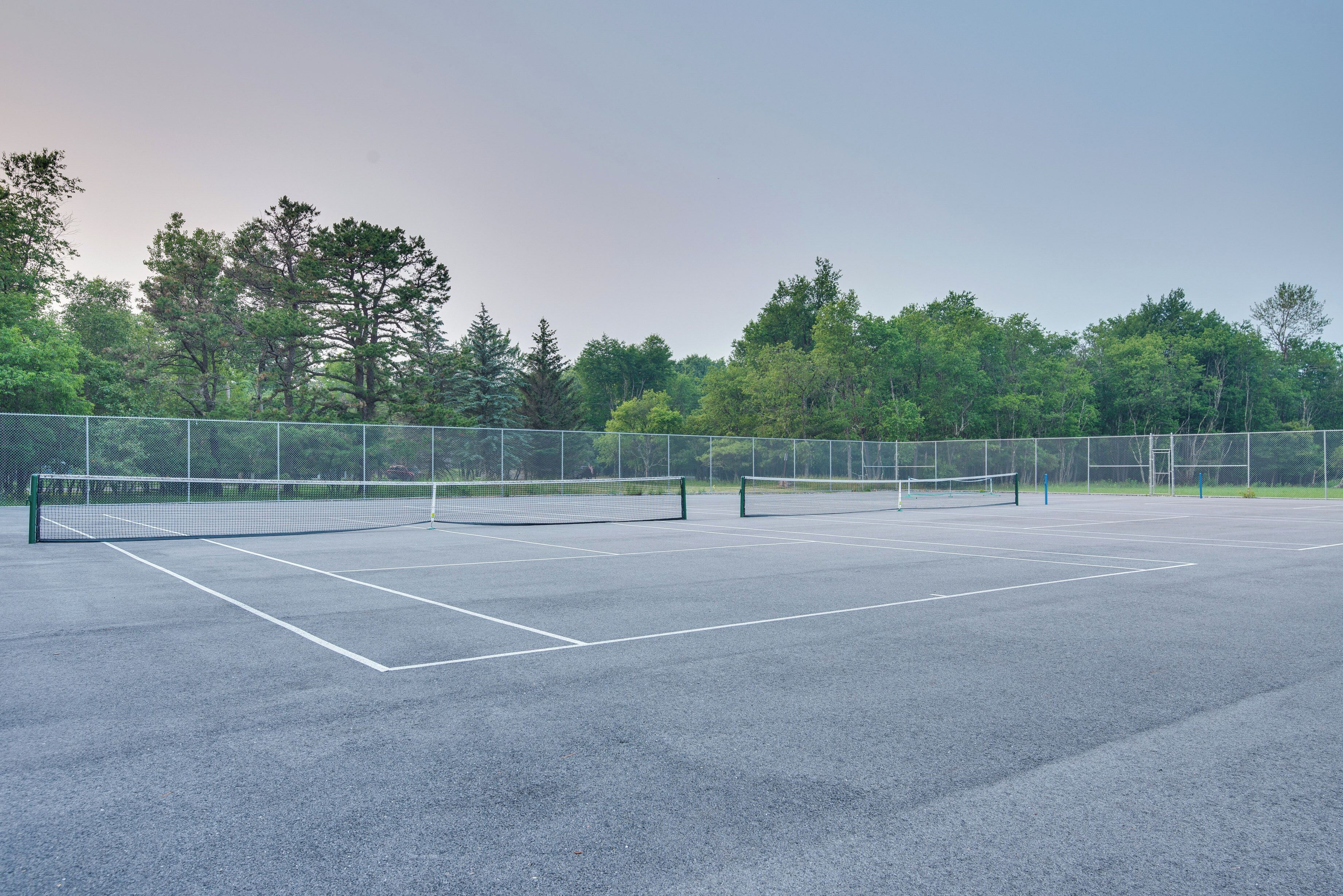 An outdoor tennis court with a net, surrounded by trees and a fence.