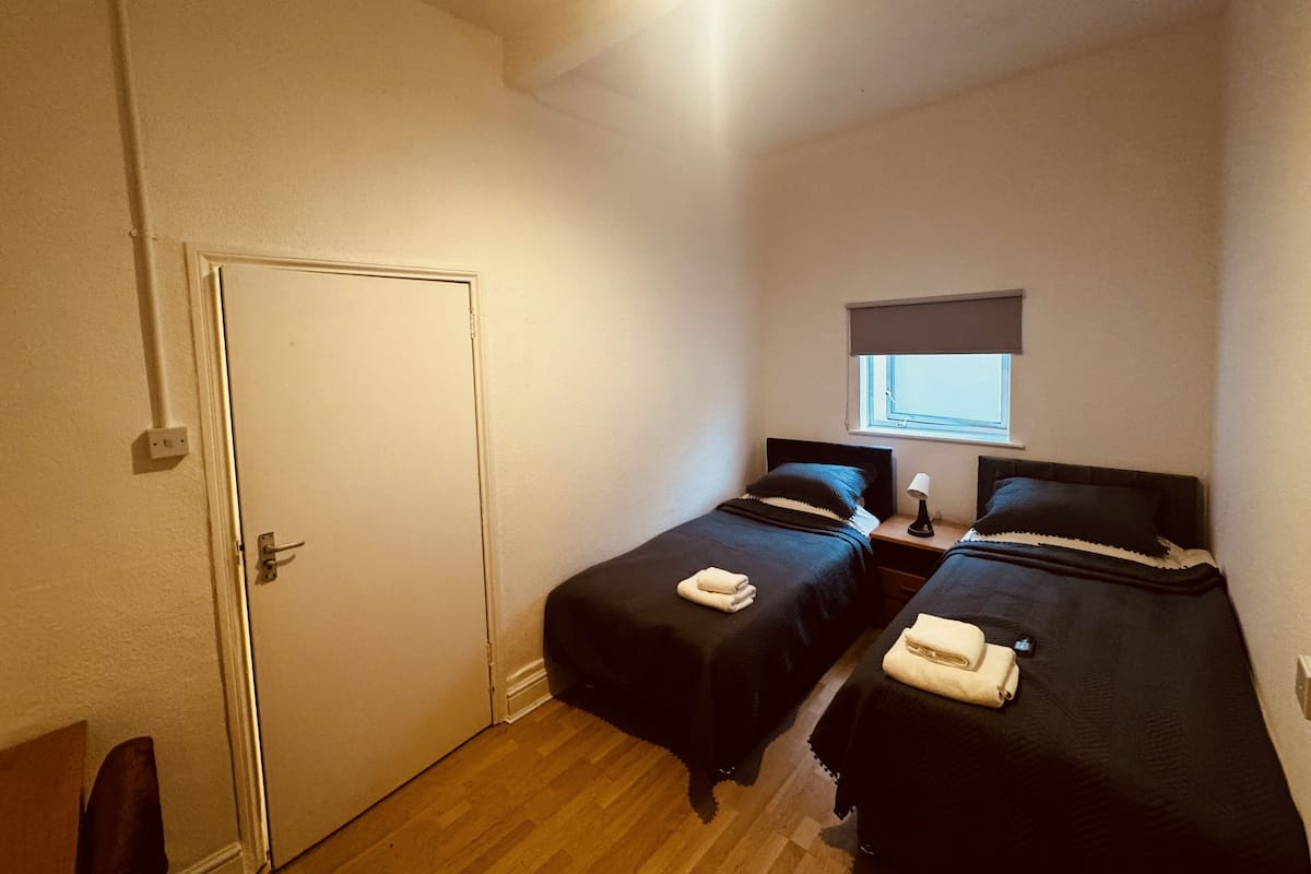 Una habitación pequeña y luminosa con dos camas, una ventana con vistas y una puerta.
