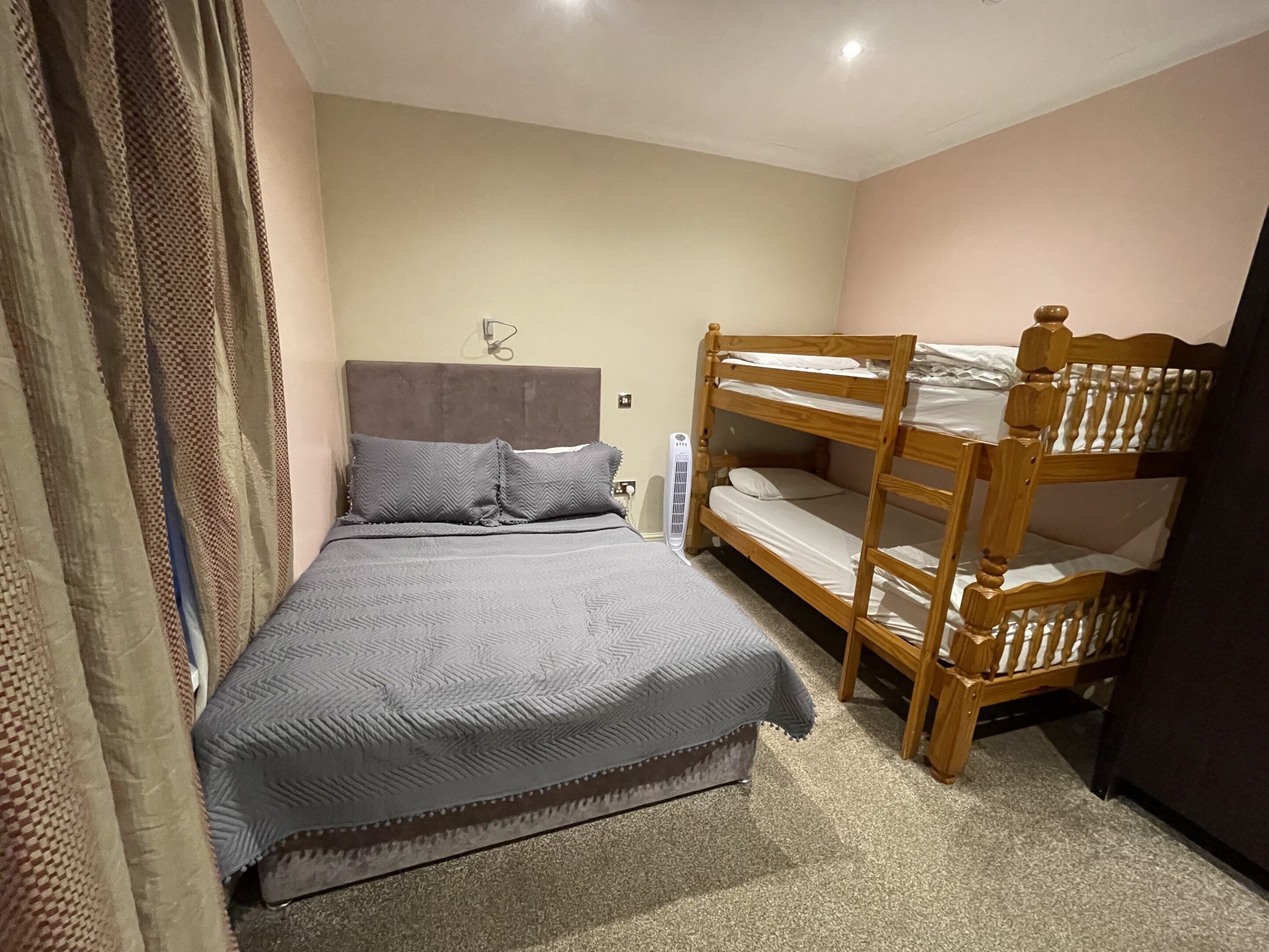 Une chambre avec un lit superposé, un lit simple, une table de chevet et une horloge murale.