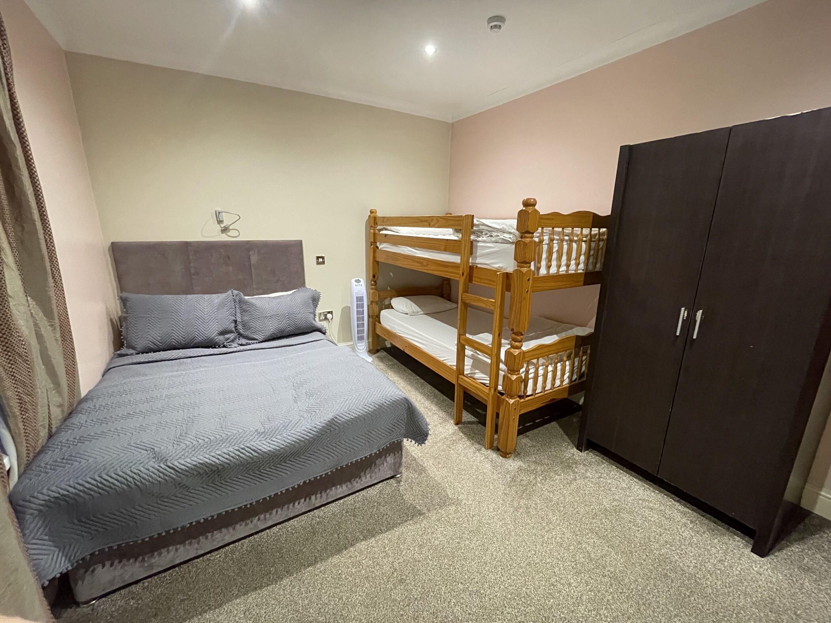 A bedroom with a bunk bed, a single bed, a wardrobe, and a ceiling fan.
