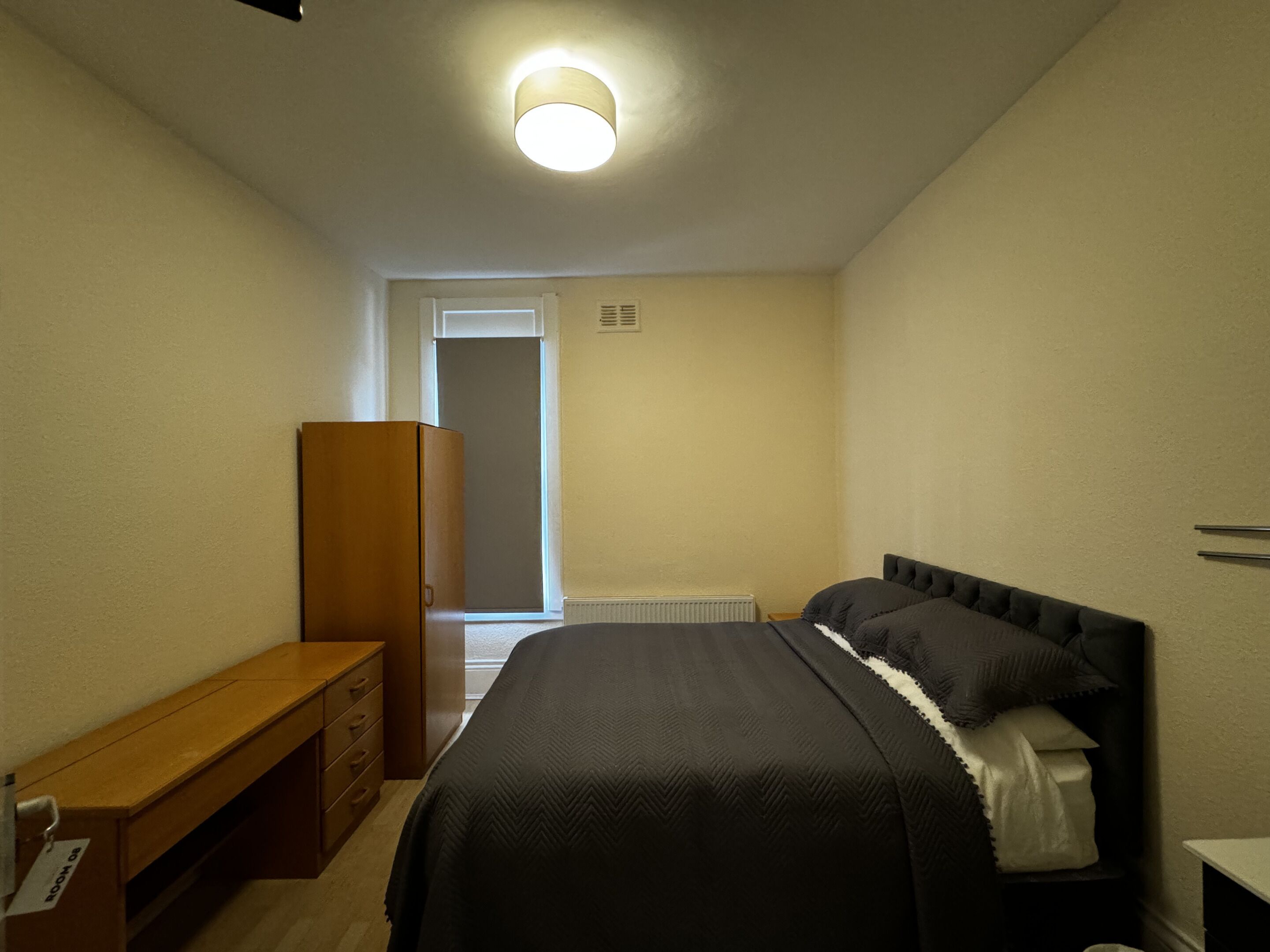 A bedroom with a bed, a wooden bench, a wardrobe, and a radiator.