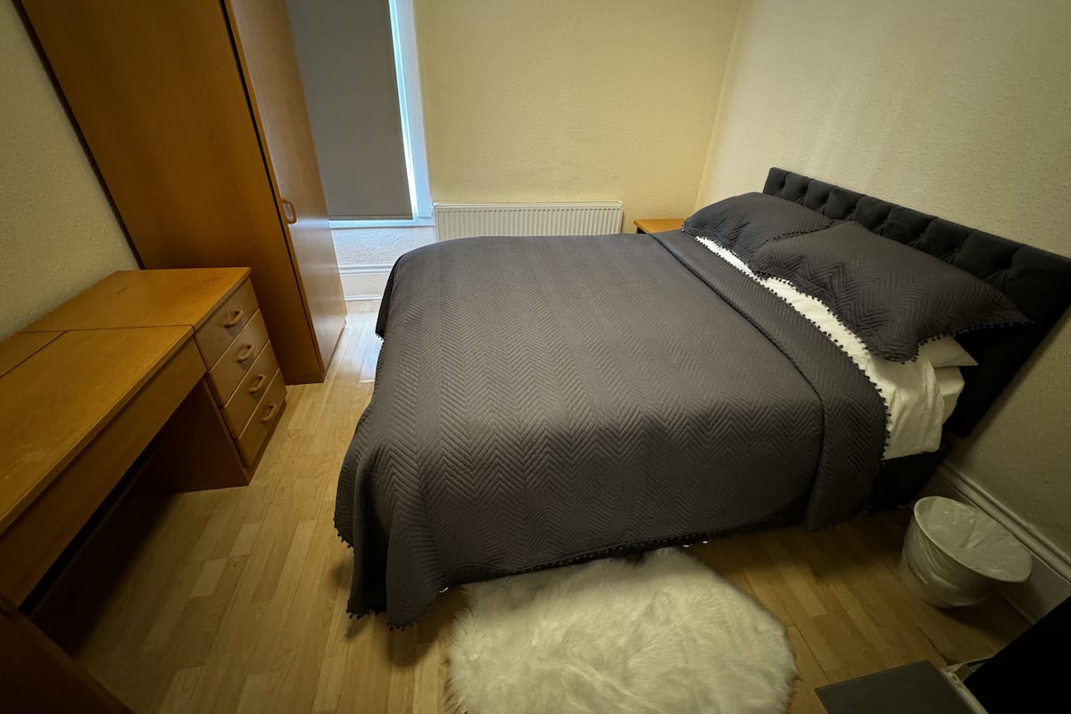 Un dormitorio con una cama, un aparador de madera, un tapete blanco y mullido, y un radiador blanco.