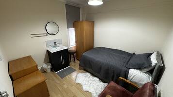 Un dormitorio con cama, un armario de madera, un escritorio pequeño con silla, un espejo y una lámpara.