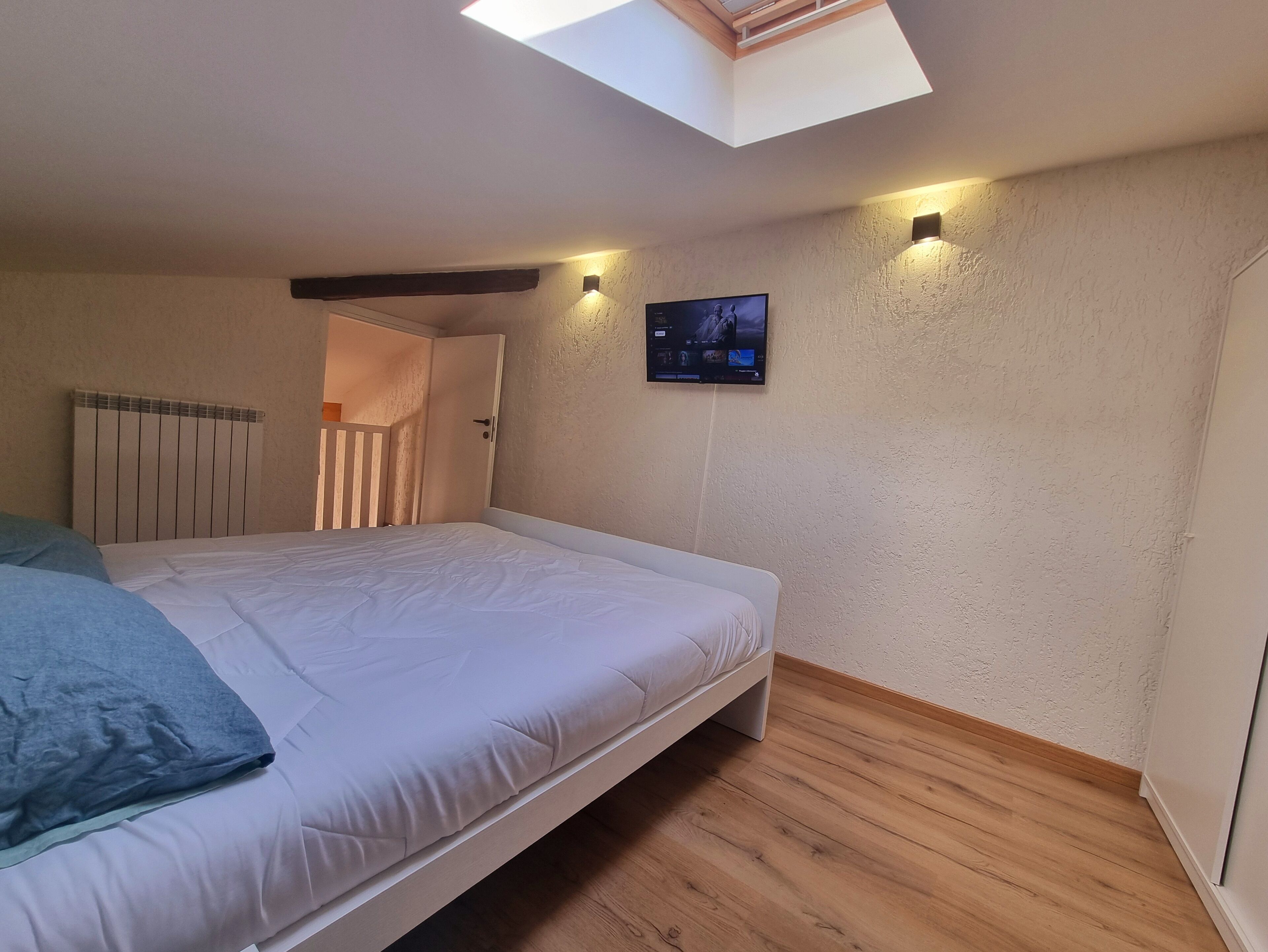 Een slaapkamer met een bed, dakraam, een tv aan de muur en een houten vloer.