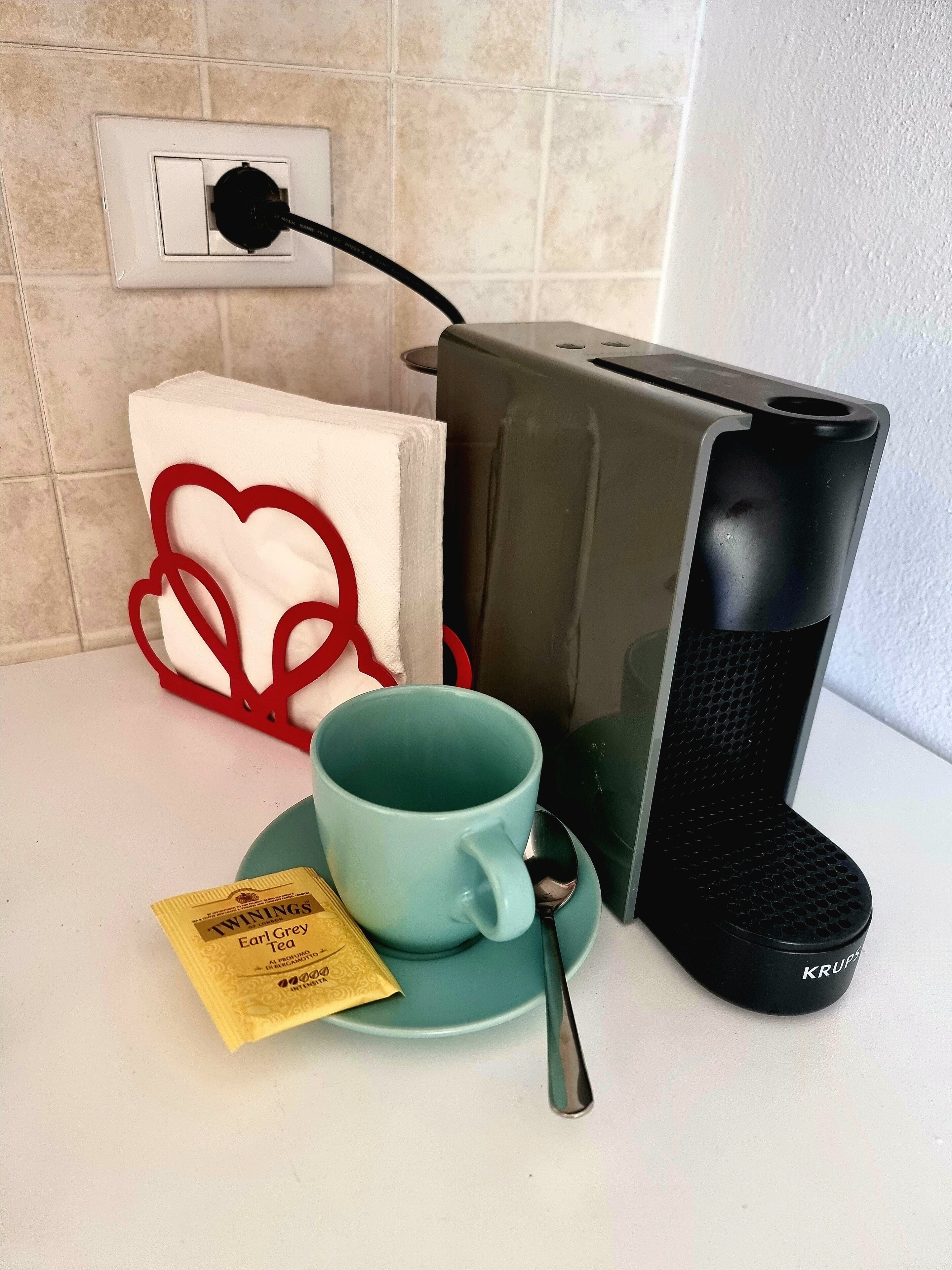 A kitchen counter with a coffee maker, a mug, a spoon, and a tea packet.