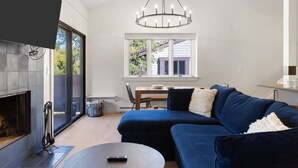 Ein modernes Wohnzimmer mit Kamin, einem blauen Sofa, einer Chandelier und einem Essbereich mit Fensterblick.