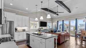 A modern kitchen with white cabinets, a large island, stainless steel appliances, pendant lighting, and a view of the backyard through large windows. - LinkedOUT #171 – 3 BD Dog Friendly Greensboro St Duplex Steps from the beach! (Wrightsville Beach)