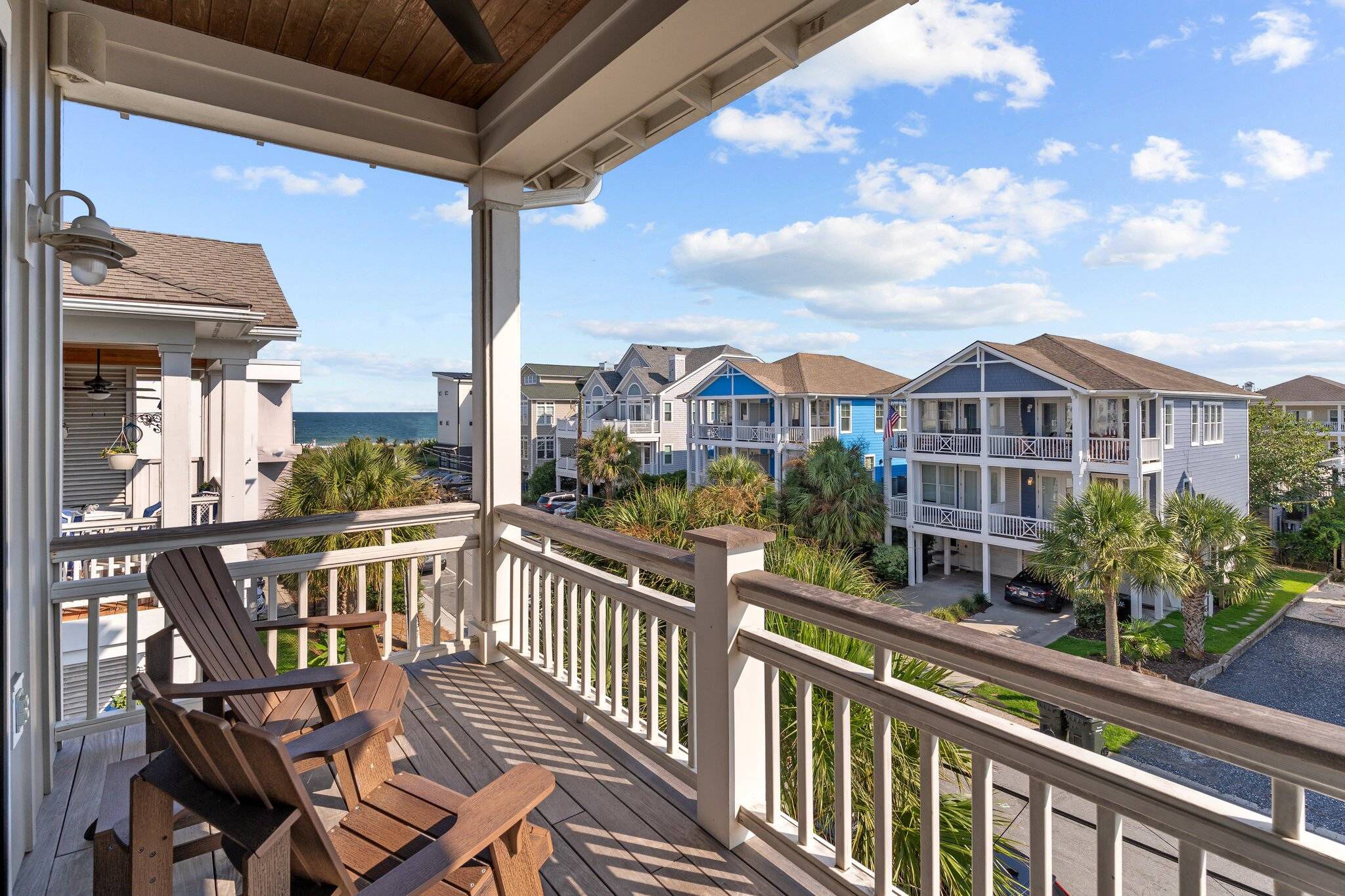A wooden deck with chairs, a railing, and a view of a coastal residential area with houses and a body of water.