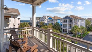 A wooden deck with chairs, a railing, and a view of a coastal residential area with houses and a body of water. - LinkedOUT #171 – 3 BD Dog Friendly Greensboro St Duplex Steps from the beach! (Wrightsville Beach)