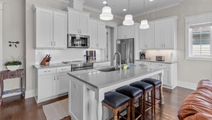 A modern kitchen with white cabinets, stainless steel appliances, and a central island with bar stools. - LinkedOUT #171 – 3 BD Dog Friendly Greensboro St Duplex Steps from the beach! (Wrightsville Beach)