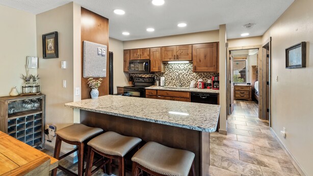 A modern kitchen with a granite island, wooden cabinets, and a microwave. - Alpine Comfort Just Steps from the Slopes – Timber Run 306! (Steamboat Springs)