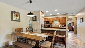 A dining area with a wooden table and benches, a kitchen with wooden cabinets, and a tiled backsplash. - Alpine Comfort Just Steps from the Slopes – Timber Run 306! (Steamboat Springs)
