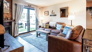 A cozy living room with a brown leather sofa, a wooden coffee table, and a fireplace. - Alpine Comfort Just Steps from the Slopes – Timber Run 306! (Steamboat Springs)