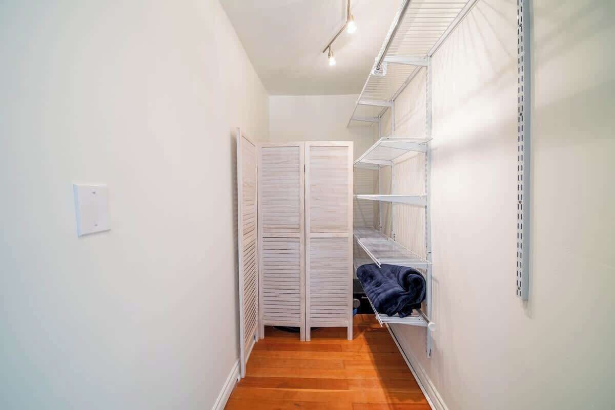 A narrow hallway with a wooden floor, white walls, and a white closet with sliding doors.