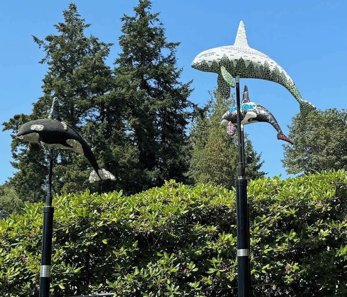 Une sculpture représentant une baleine et un dauphin, fixée sur un poteau, et entourée de verdure et d’arbres.