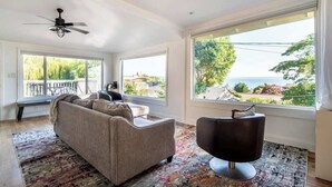 A spacious living room with a large window, a ceiling fan, and a modern chair. - Orca Haven: 2BR w/ Scenic Views, Richmond Beach (Shoreline)