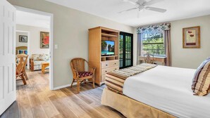 Une chambre à coucher comprenant un lit, une armoire en bois, un téléviseur, un ventilateur de plafond, une fenêtre avec des rideaux et une chaise.