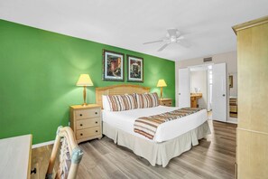 A bedroom with a bed, two bedside lamps, a ceiling fan, and two framed pictures on the wall.