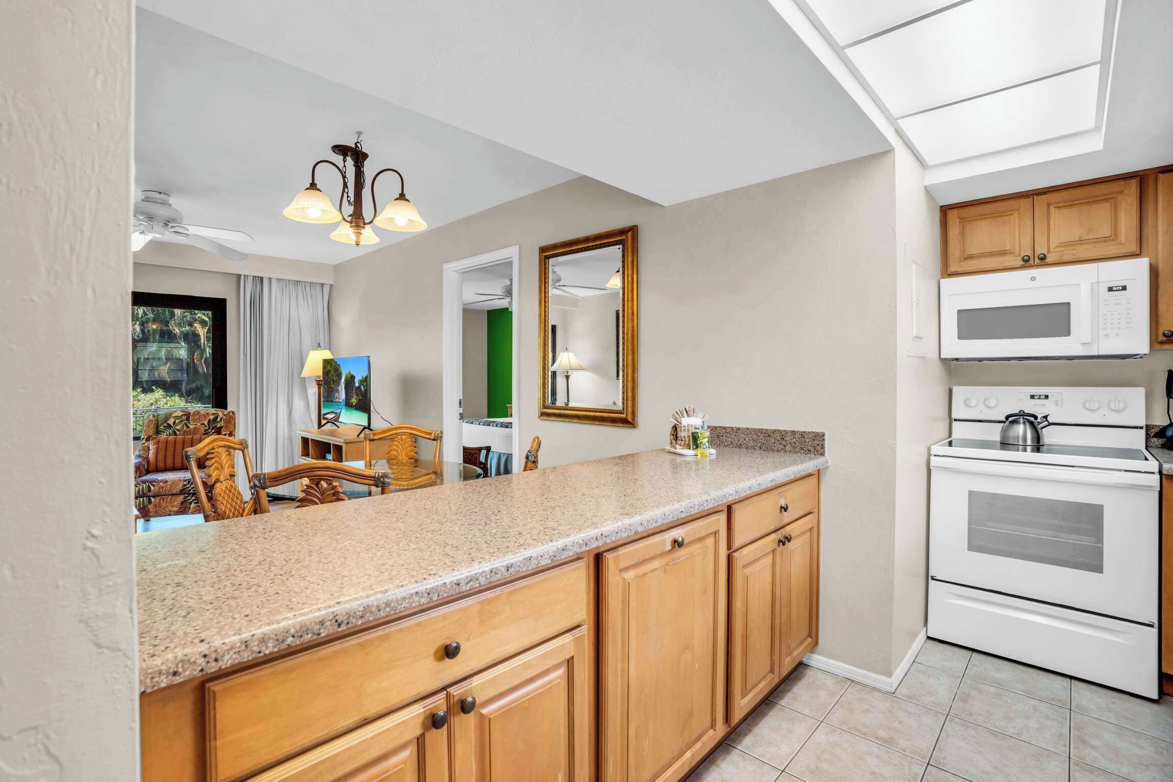 A modern kitchen with wooden cabinets, a granite countertop, a microwave, an oven, and a ceiling fan.