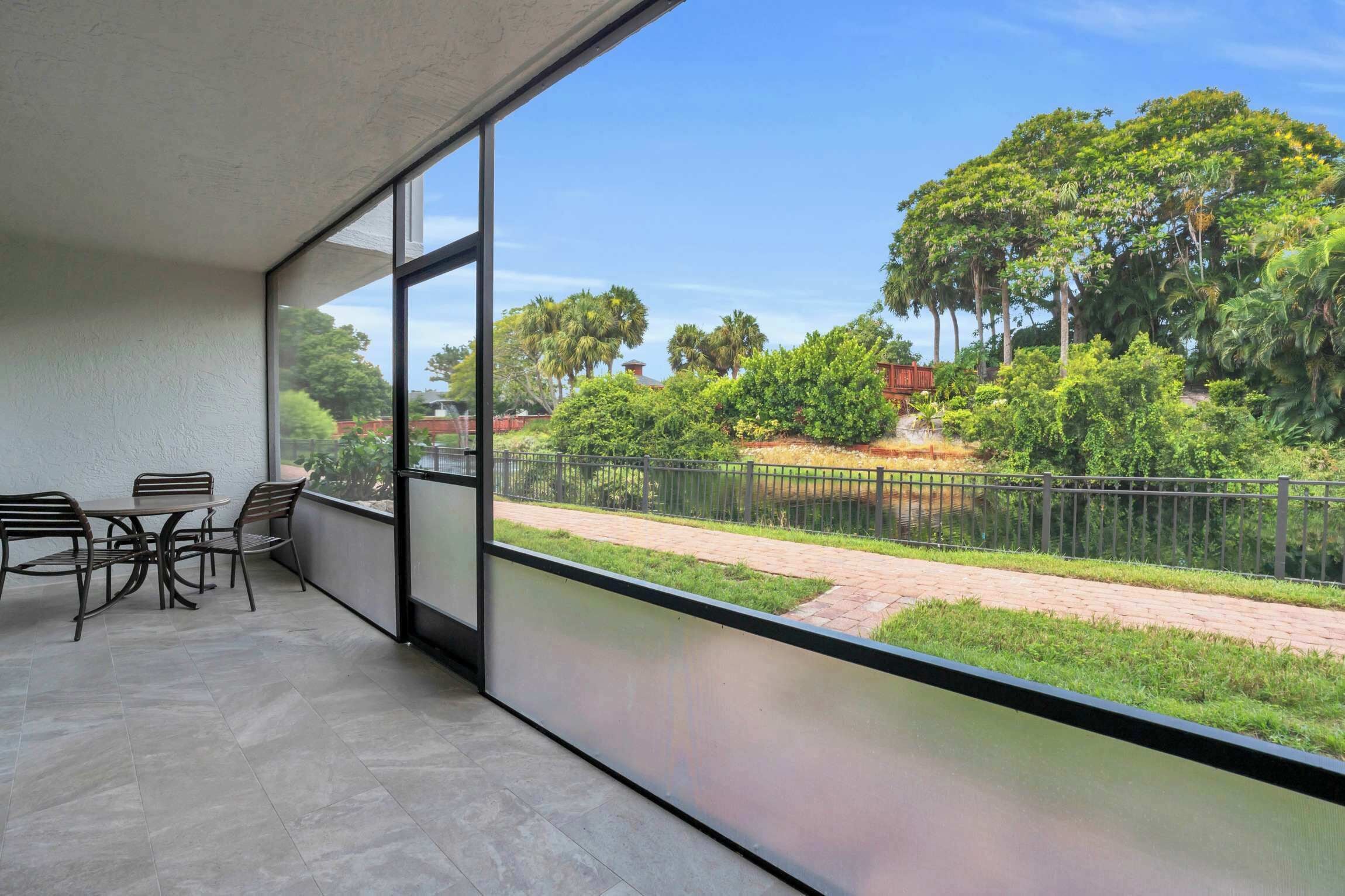 A balcony with a table and chairs, overlooking a landscaped garden with a pathway and a fence.