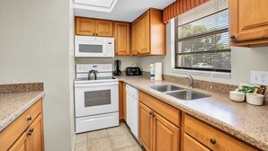 Une cuisine dotée de meubles en bois, d’un four à micro-ondes, d’une cuisinière, d’un lave-vaisselle et d’une fenêtre avec des stores.