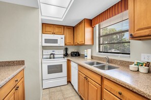 A kitchen with wooden cabinets, a microwave, a stove, a dishwasher, and a window with blinds.