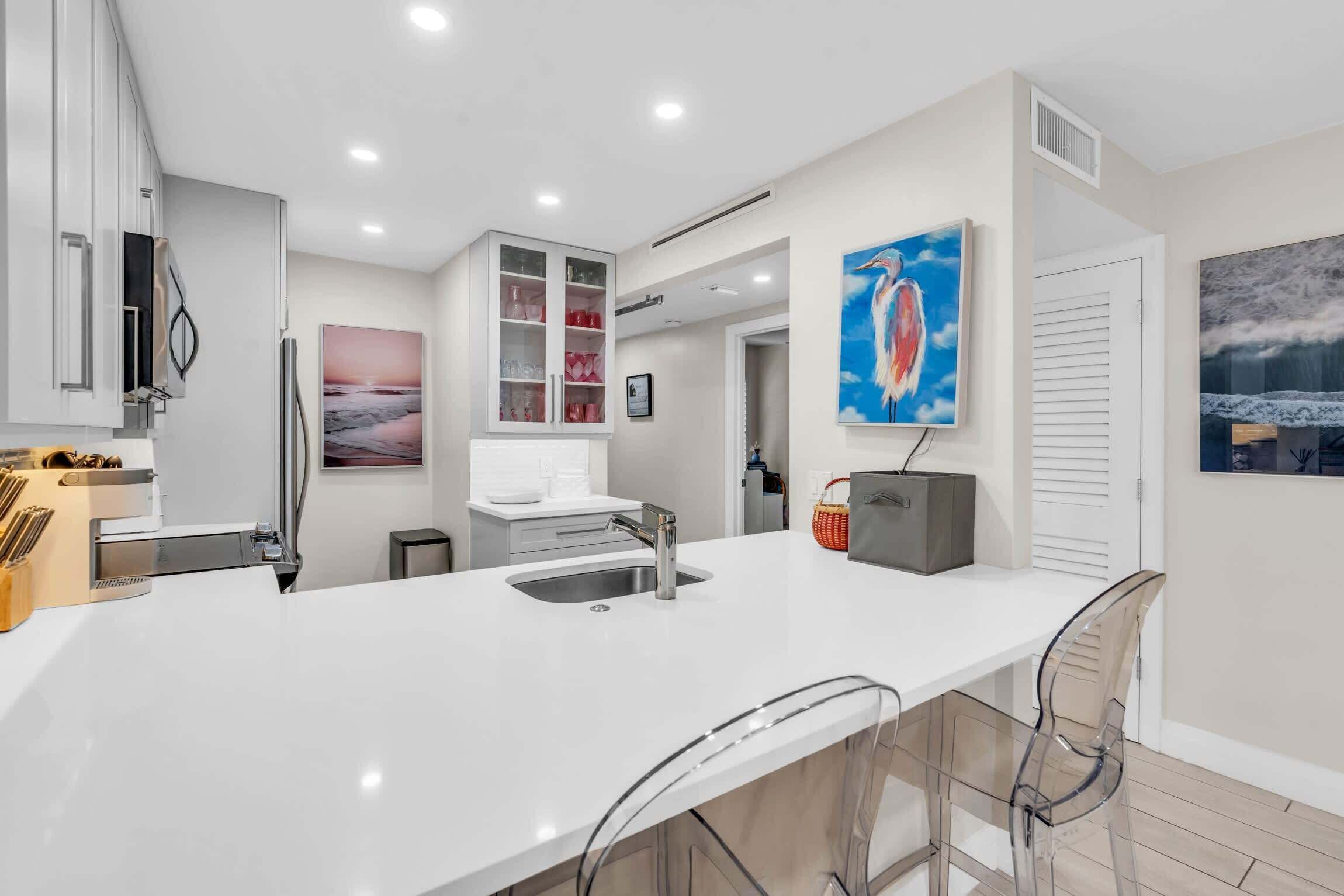 A modern kitchen with a central island, bar stools, and a dining area.