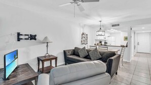 Un soggiorno moderno con un divano grigio, una poltrona bianca, un tavolino in legno, una televisione e una ventola a soffitto.