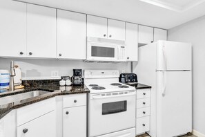 A modern kitchen with white cabinets, a built-in microwave, a stove, a refrigerator, and a coffee maker.