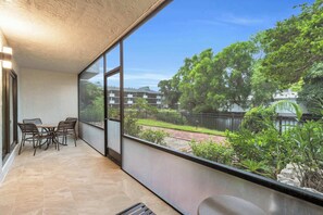 Varanda com mesa e cadeiras, vista para área residencial com árvores e cerca.