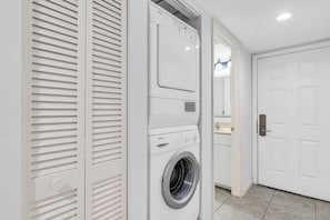 A laundry room with a front-loading washing machine and dryer, a white door, and a tiled floor.