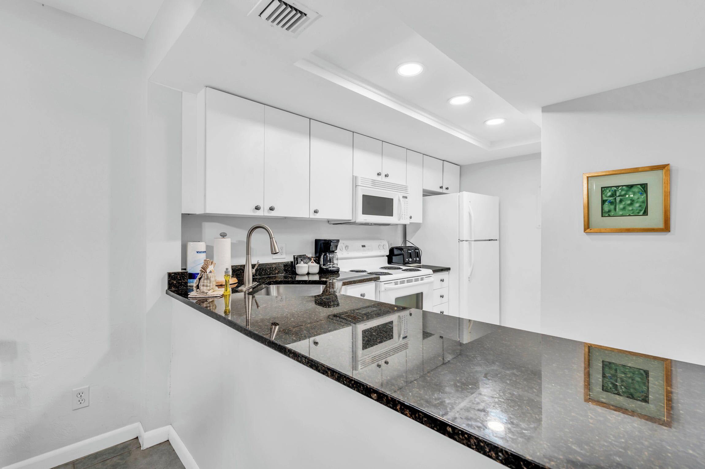 A modern kitchen with white cabinets, a granite countertop, and stainless steel appliances.